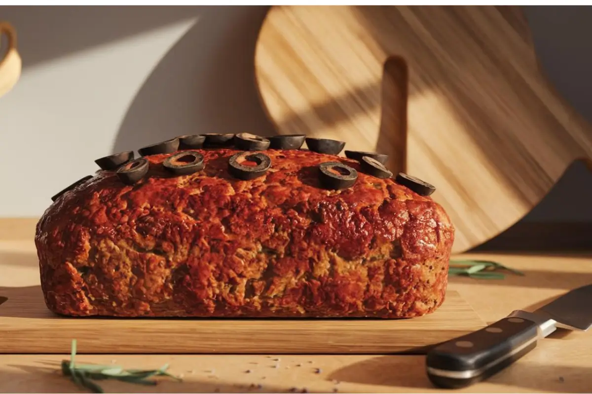 Close-up of a meatloaf crumbling as it is sliced on a cutting board.